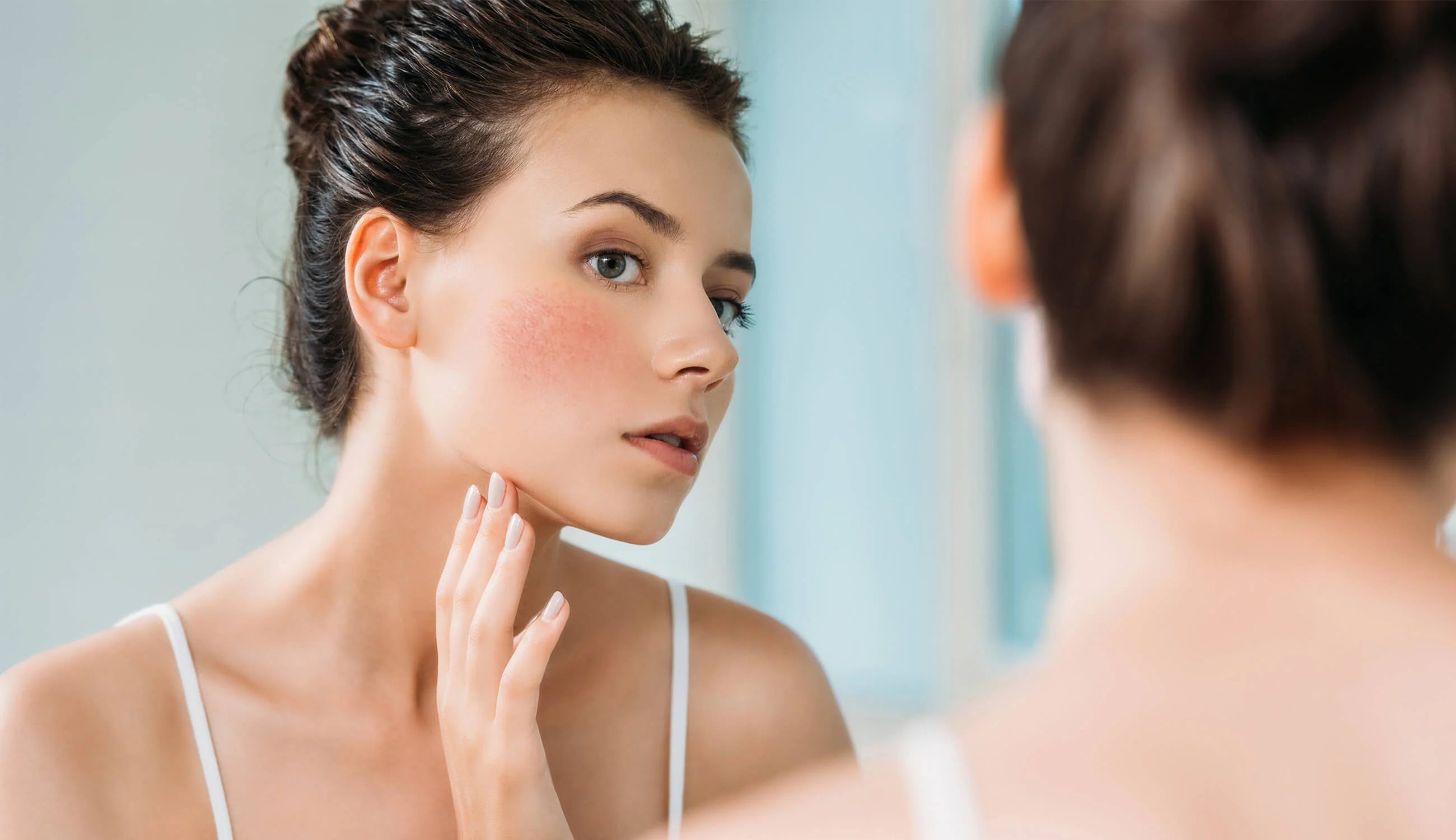 Woman examining her face in a mirror.